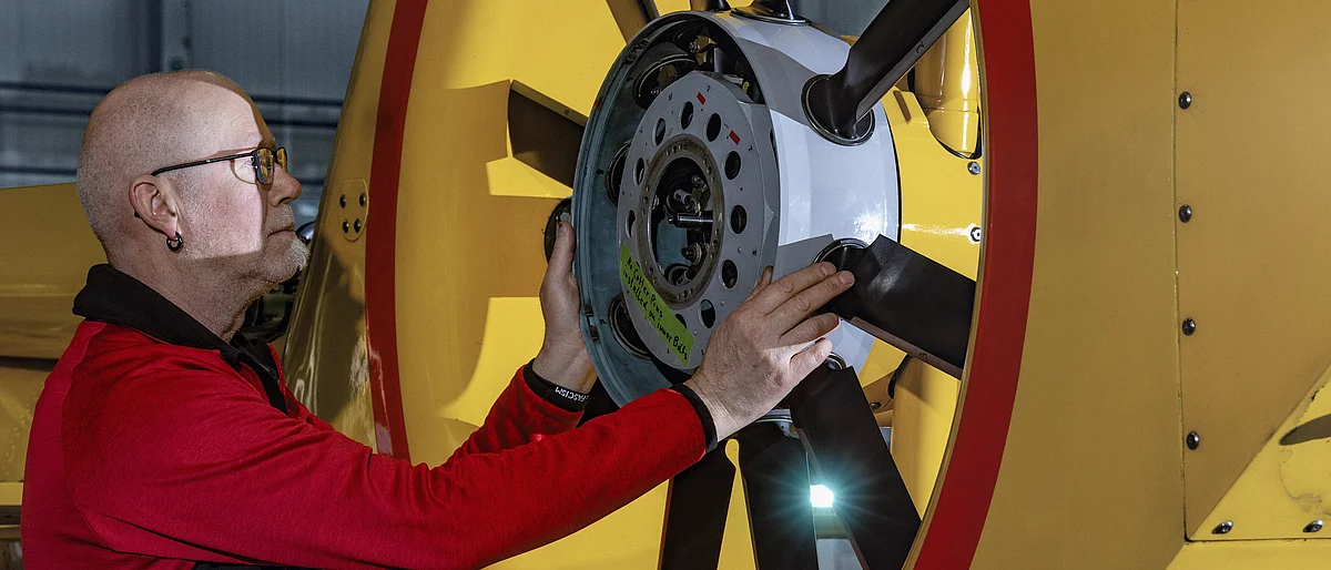 An aircraft mechanic works on the Fenestron of a yellow helicopter.