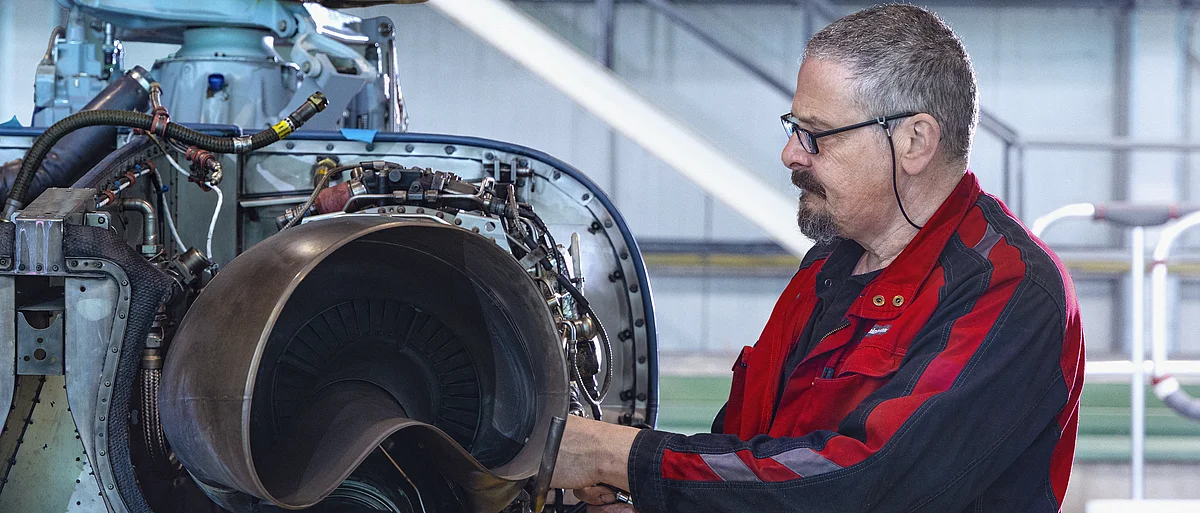 [Translate to English:] Eine Fluggerätmechaniker arbeitet an einem Triebwerk eines Hubschraubers.